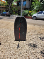 Load image into Gallery viewer, Black bodyboard with red side trim standing upright on gravel in Nosara, Costa Rica.
