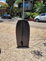 Load image into Gallery viewer, Black bodyboard standing upright on gravel, available for rent at The Frog Pad in Playa Guiones.