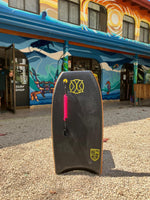 Load image into Gallery viewer, Dark bodyboard with colorful graphics and leash, photographed outside The Frog Pad surf shop.